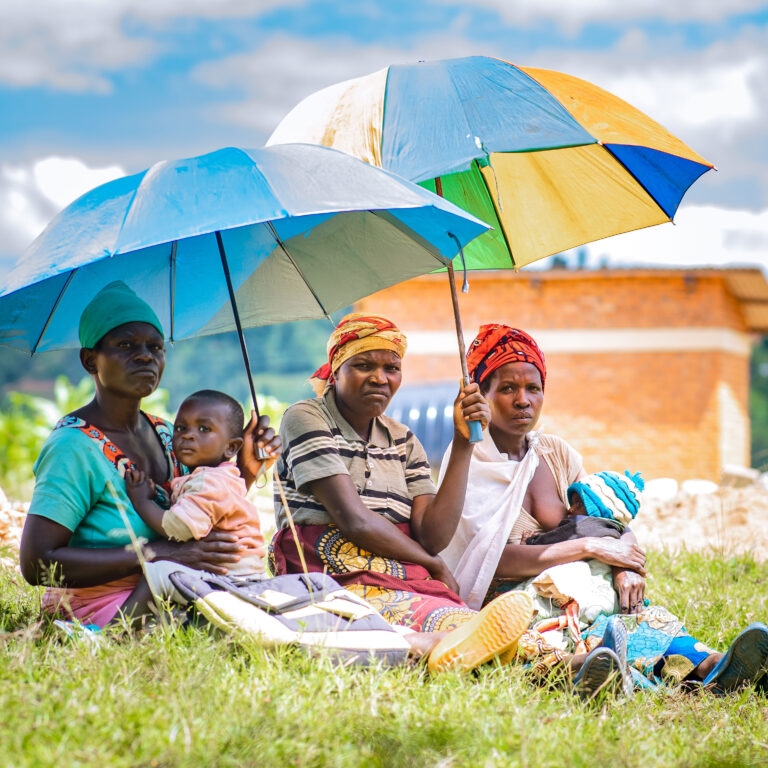 Women and their children sit under the shade of umbrellas